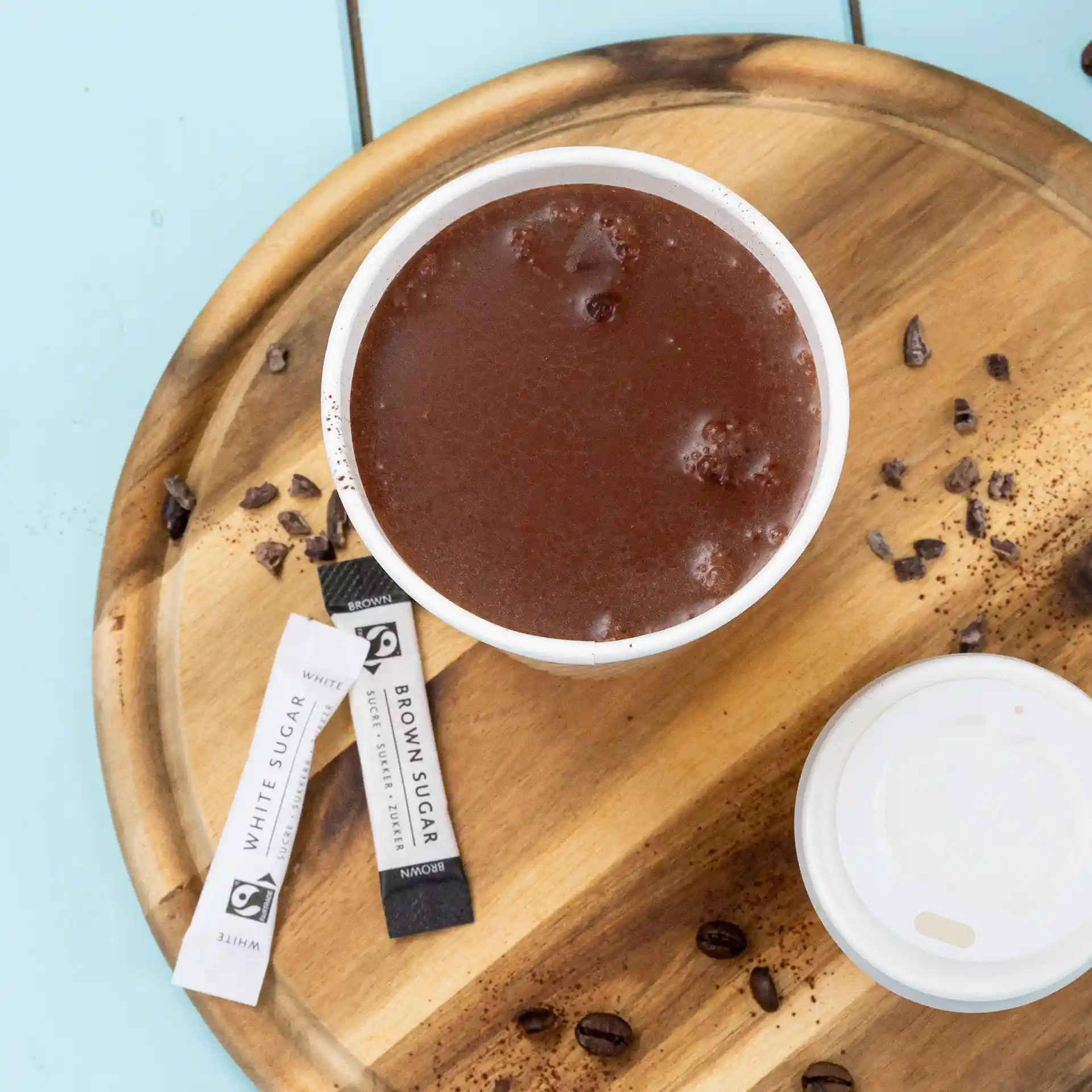 Tazza di cioccolata calda su un vassoio di legno con bastoncini di zucchero e chicchi di caffè sparsi.