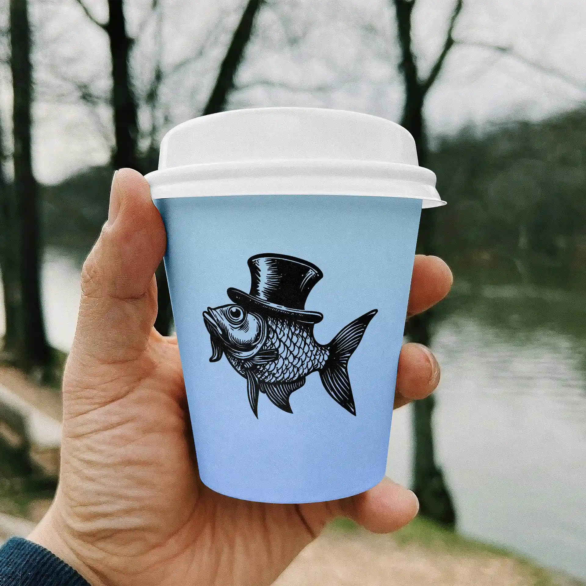 Mano che tiene un bicchiere di carta azzurro chiaro con un'illustrazione nera di un pesce con un cilindro, con sfondo sfocato.