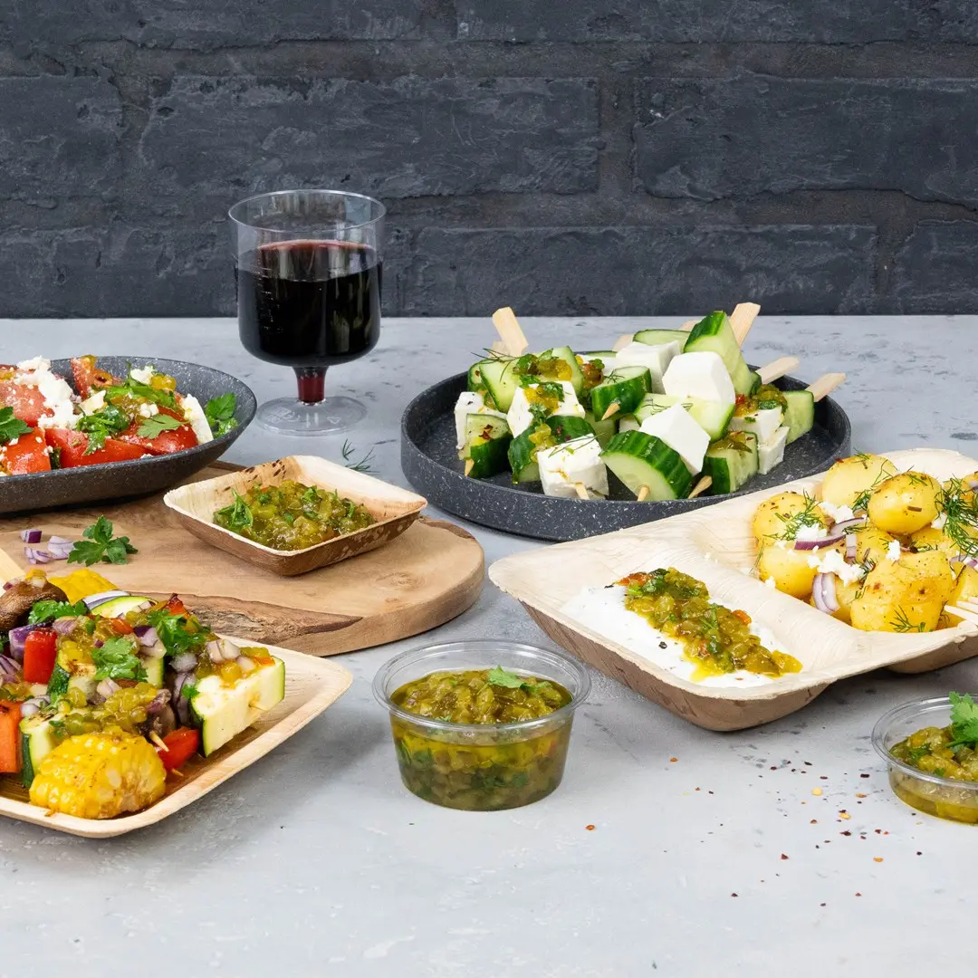 Una varietà di finger food tra cui insalate, spiedini di cetriolo e formaggio e salse, con un bicchiere di vino rosso sullo sfondo.