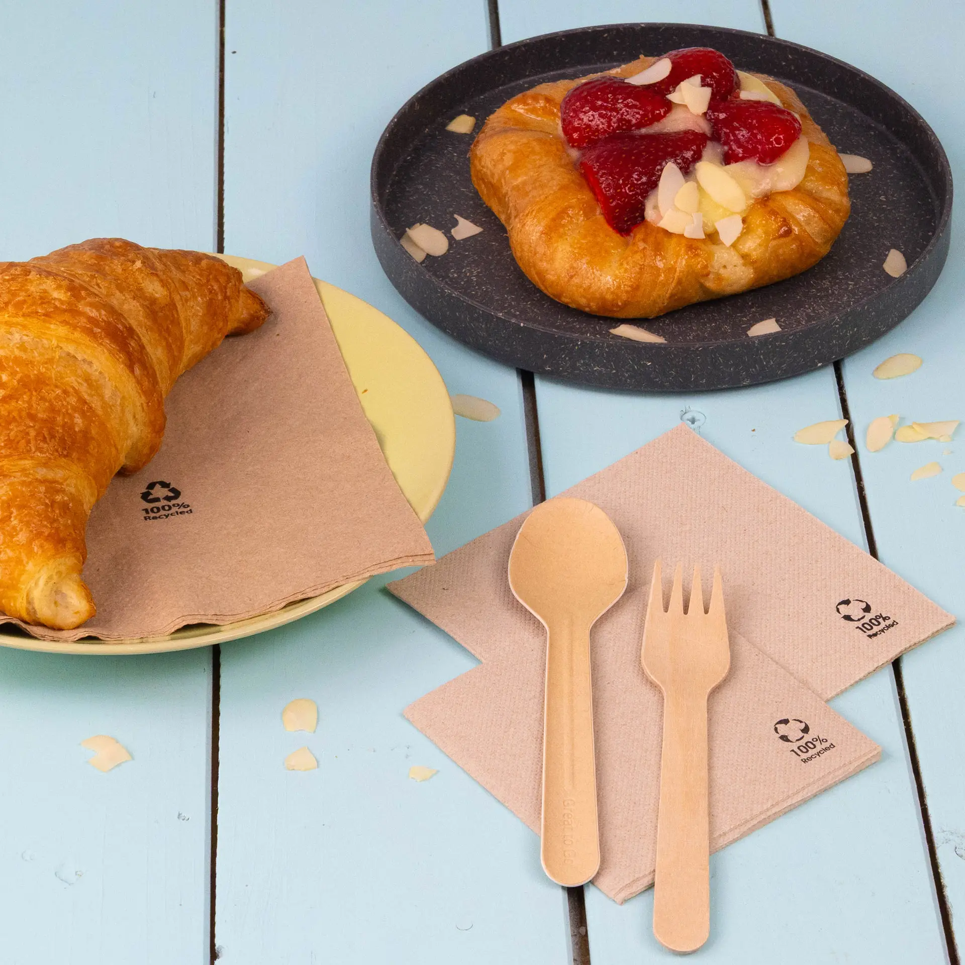 Una tazza da caffè bianca con un biscotto su un piatto bianco, circondata da una ciotola di lamponi e tovaglioli di carta riciclata.