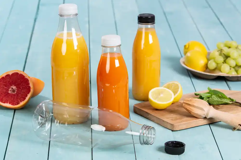 Due bottiglie di vetro piene di succo d'arancia e succo giallo, un limone tagliato, uva e metà pompelmo su una superficie di legno.
