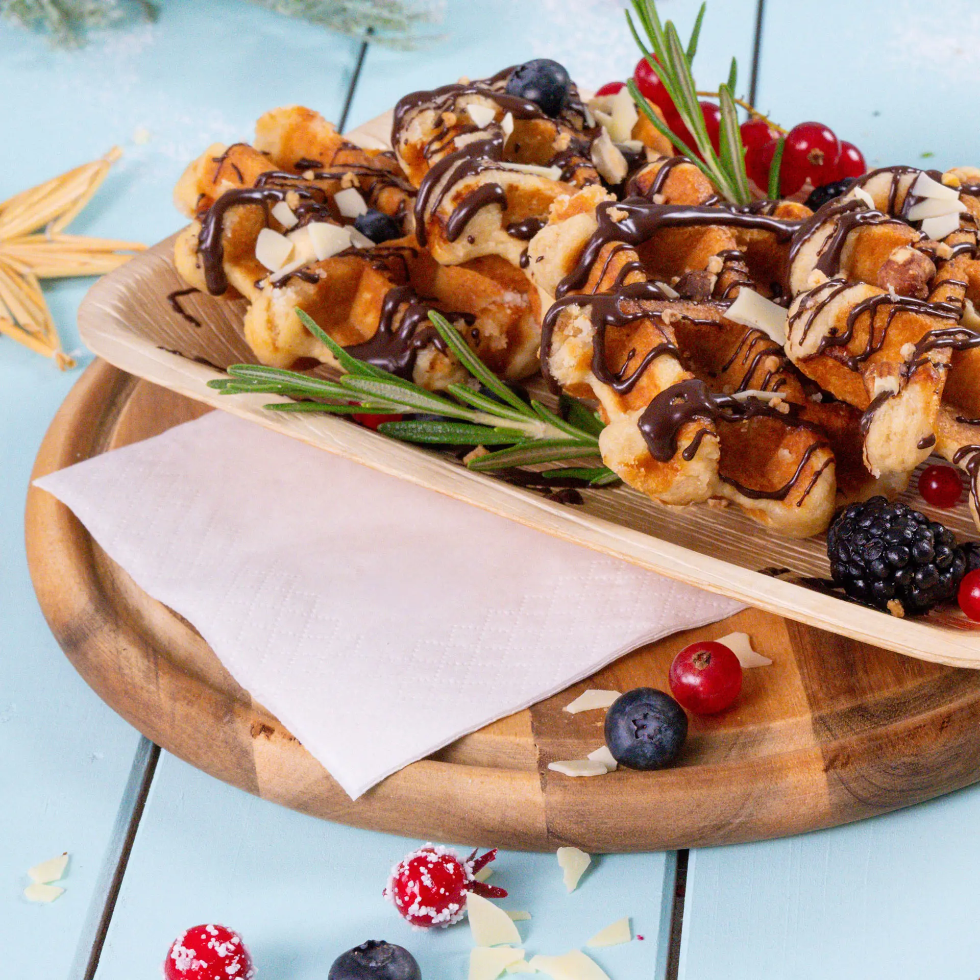 Piatto di waffle guarnito con cioccolato, noci e bacche, con un tovagliolo bianco su un tagliere di legno.