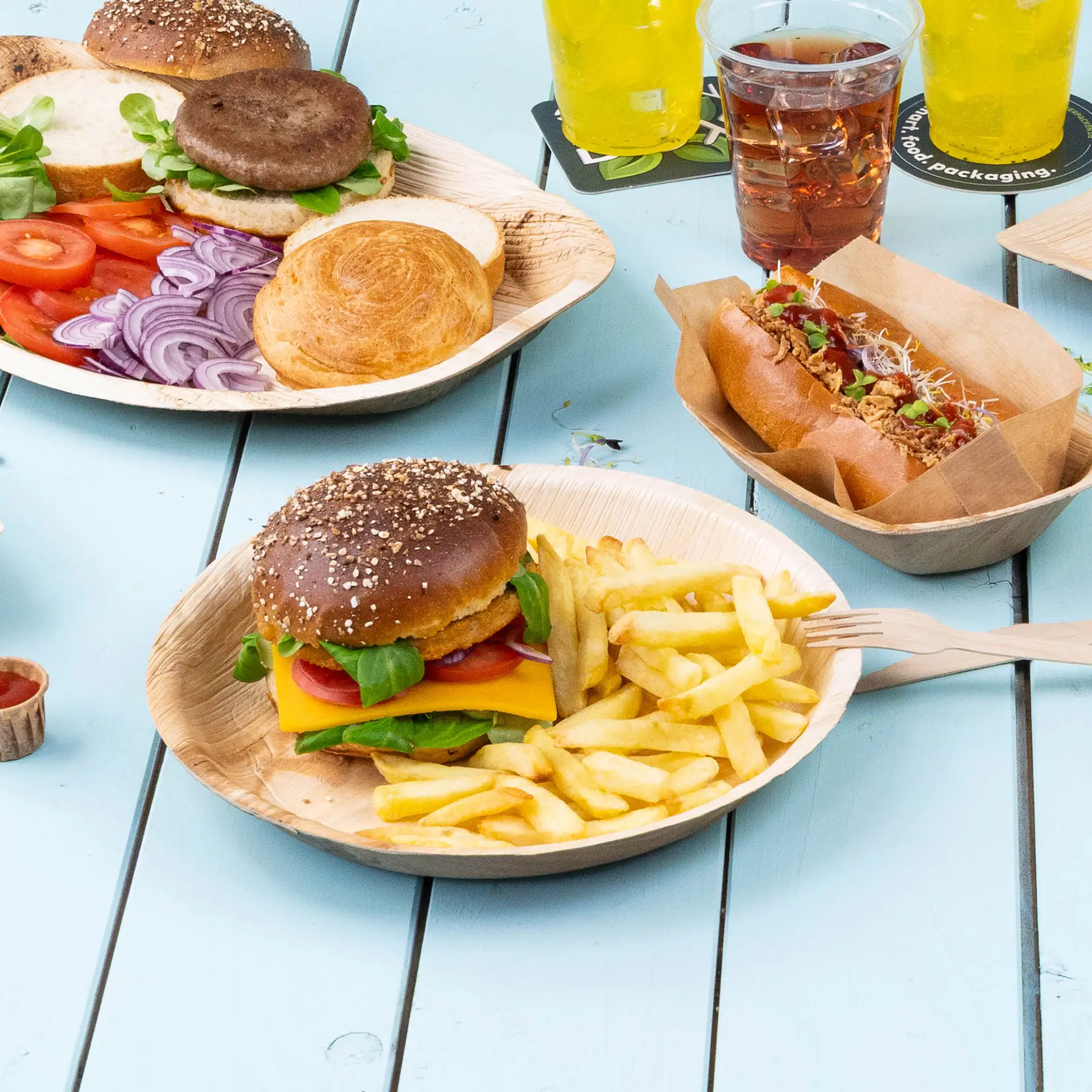 Un piatto di foglie di palma contiene un cheeseburger con lattuga, pomodoro e patatine, accanto a fette di verdure e un hot dog.