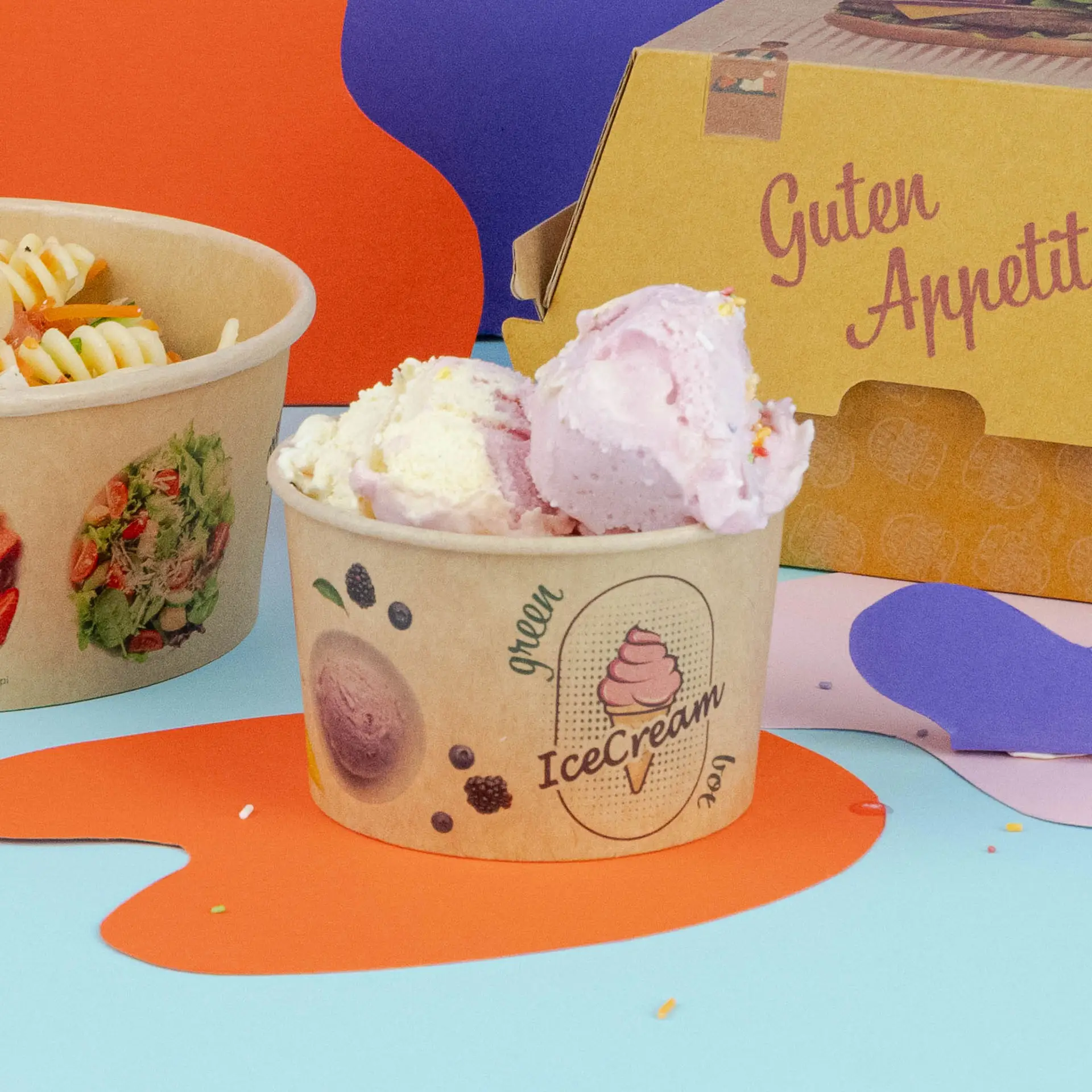 Coppa di gelato marrone con palline di gelato rosa e bianche, accanto a una ciotola di pasta e una scatola da asporto.