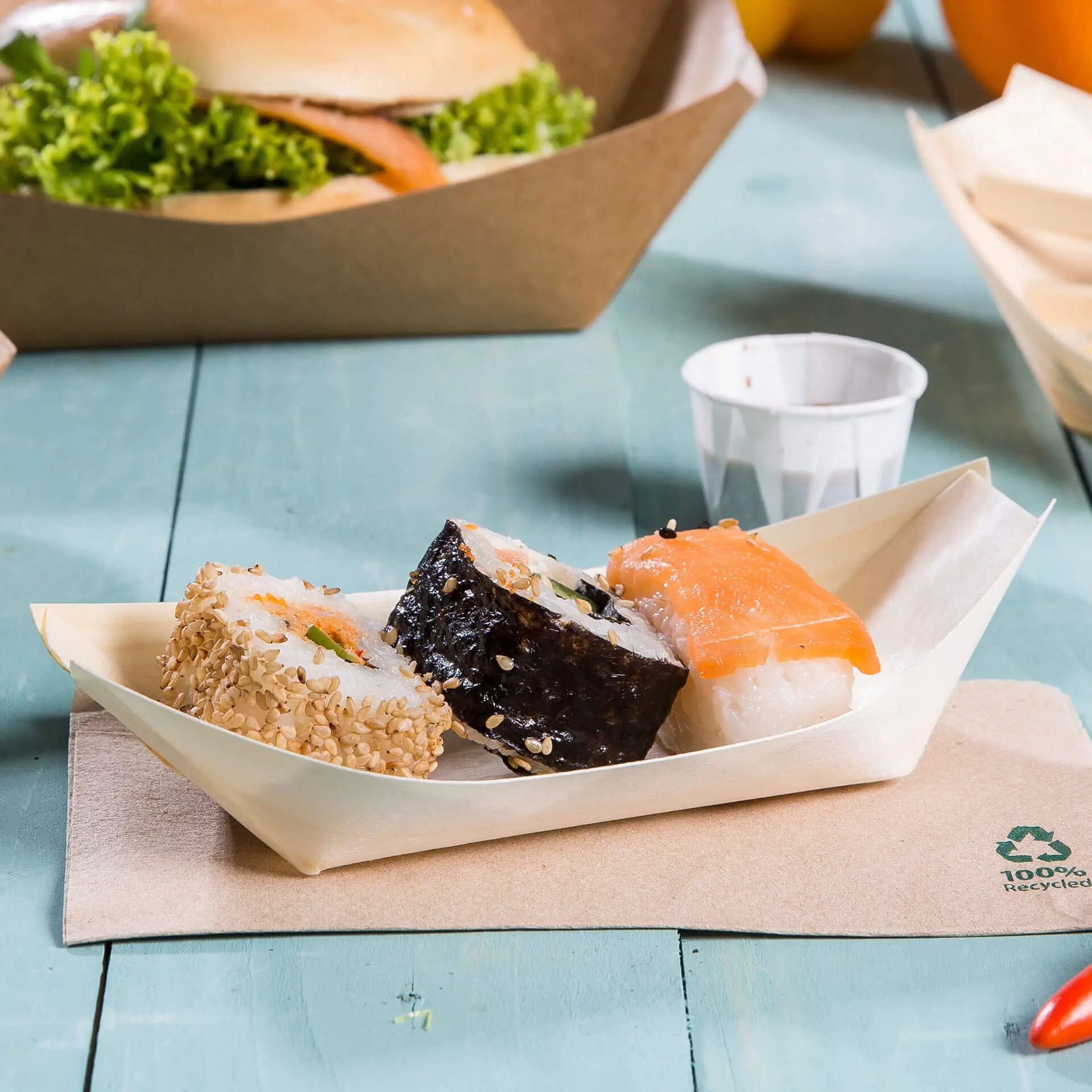 Tre pezzi di sushi disposti in una barca di legno; include un rotolo di sushi al sesamo, un rotolo di sushi nori e una fetta di salmone.