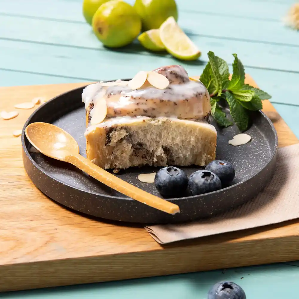 Fetta di dessert su un piatto scuro con mirtilli, fette di mandorle, un cucchiaio di legno e foglie di menta fresca.