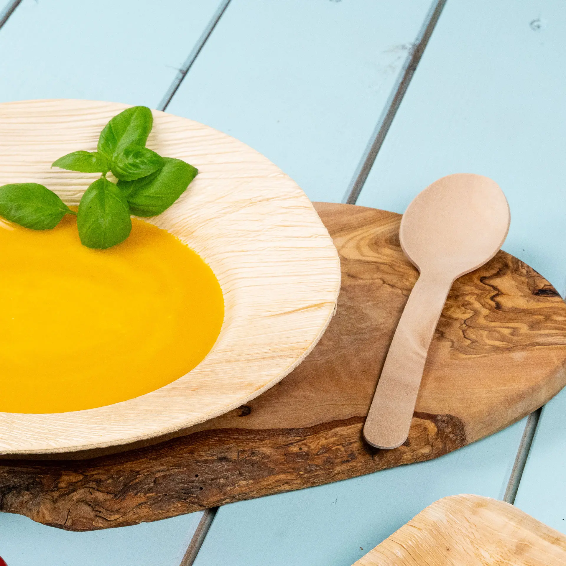 Ciotola con zuppa gialla e una foglia di basilico, accompagnata da un cucchiaio di legno su un tagliere di legno.