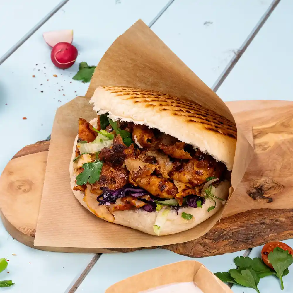 Un panino pita farcito con pollo grigliato, lattuga, cavolo rosso e coriandolo su un tagliere di legno.