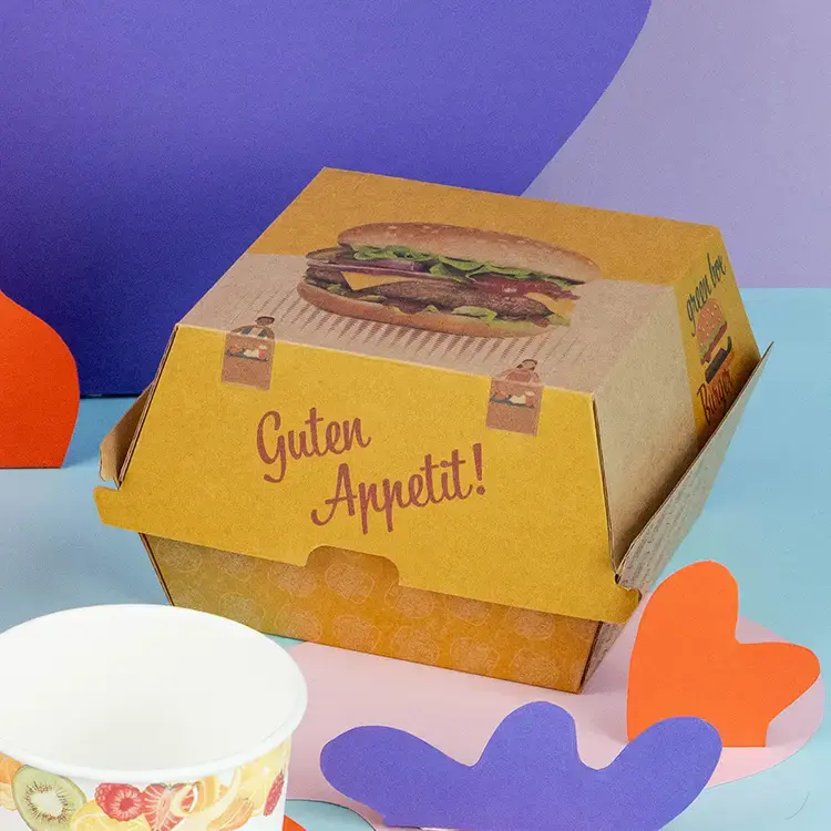 Scatole per hamburger marroni e bianche con il testo "BURGER", un hamburger con pane ai semi di sesamo e patatine su una superficie di legno.
