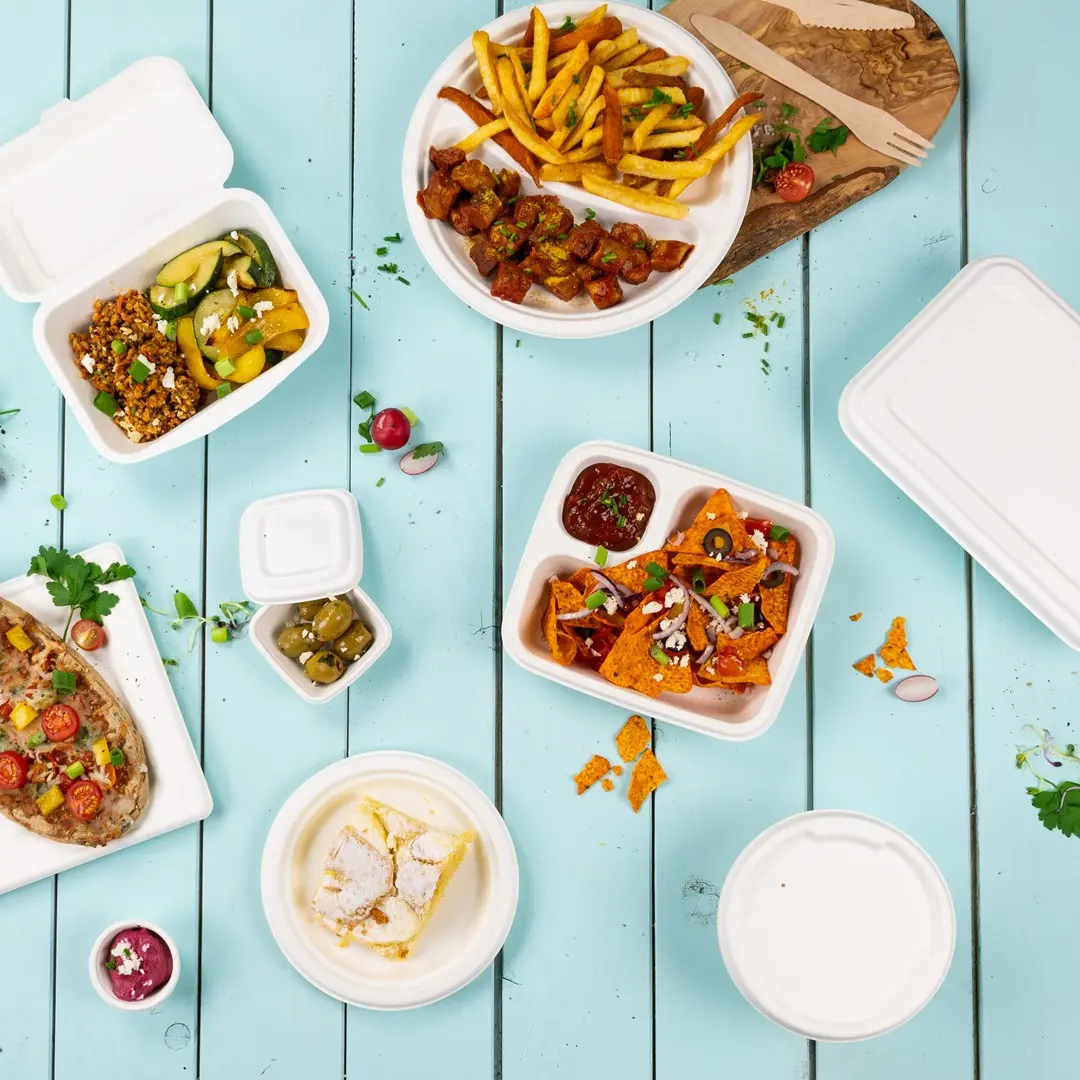 Alimenti assortiti in contenitori da asporto su una superficie in legno blu, tra cui patatine, nachos e un dessert.