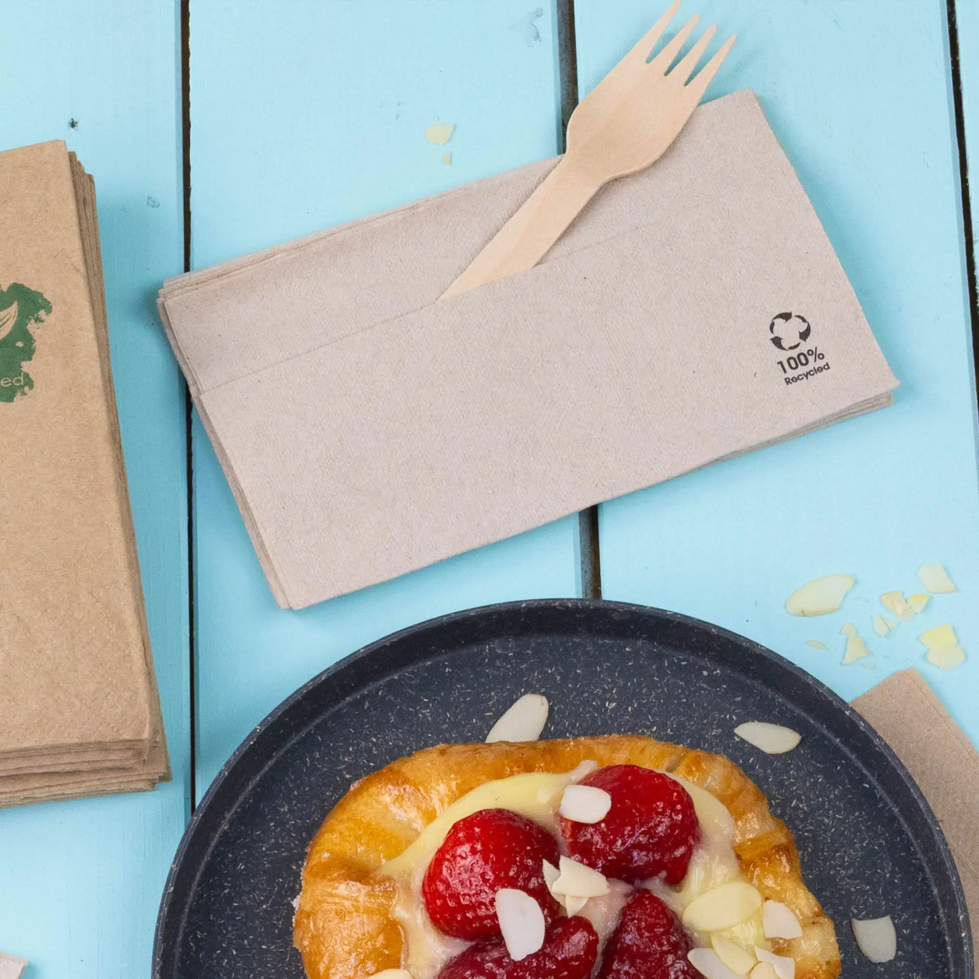 Servietta di carta riciclata con una forchetta di legno, posizionata accanto a un dolce su una superficie blu.