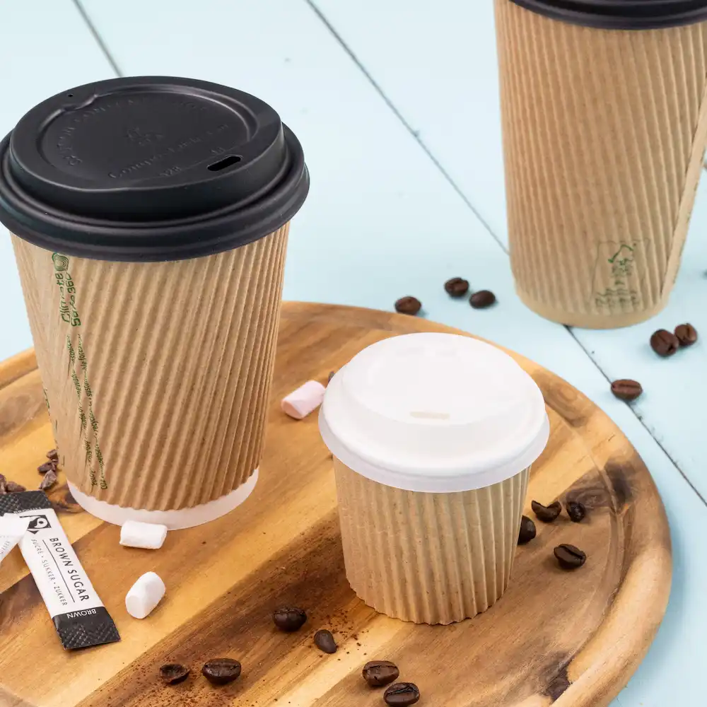 Tre tazze di carta di diverse dimensioni con coperchi, posizionate su un vassoio di legno con chicchi di caffè e bustine di zucchero.