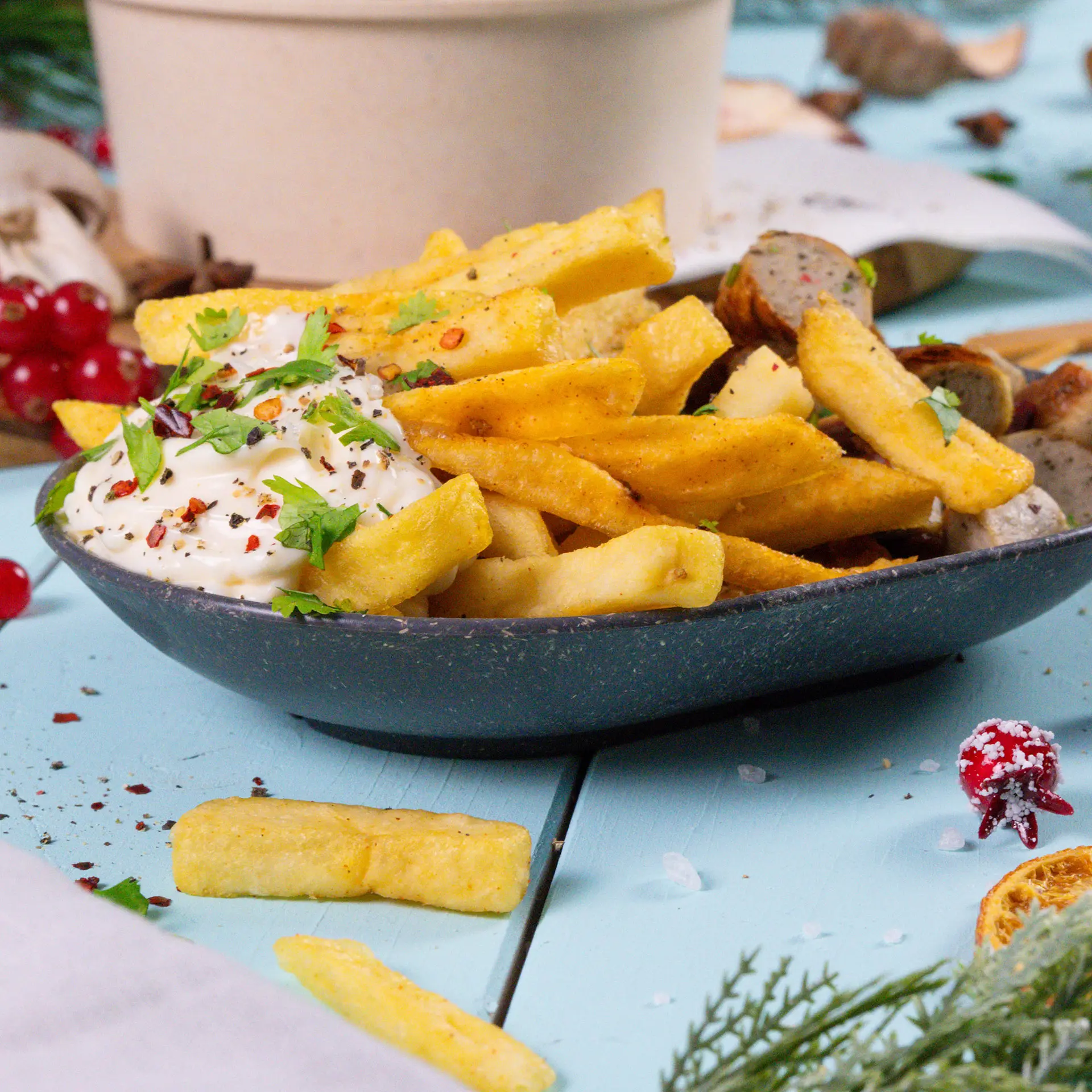 Una ciotola ovale riutilizzabile per snack piena di patatine fritte guarnite con peperoncini rossi e coriandolo; accanto ci sono peperoni verdi e rossi, una forchetta e snack.