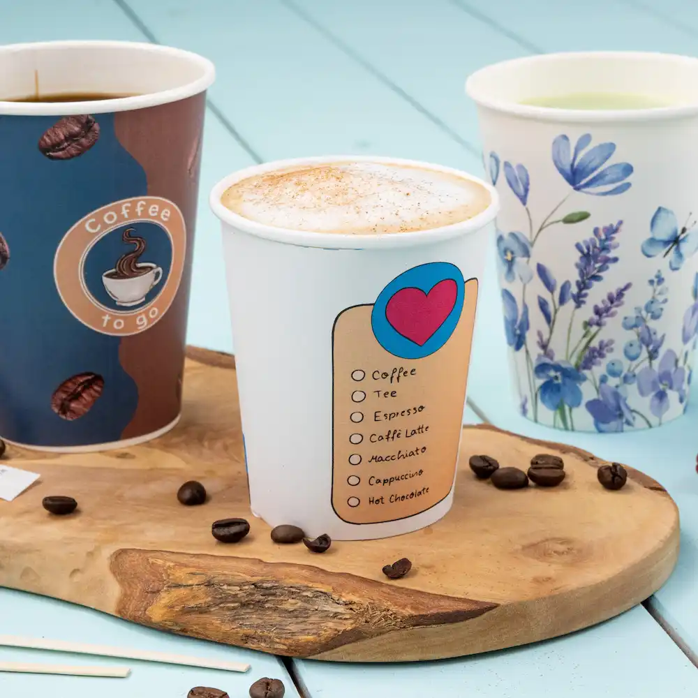 Tre bicchieri di carta pieni di bevande, tra cui un bicchiere di caffè con un elenco di opzioni di bevande, su una superficie di legno.