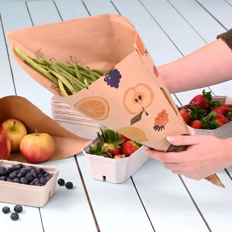 Una persona tiene un cono di fagiolini verdi, con fragole e mele sullo sfondo e un contenitore di mirtilli vicino.