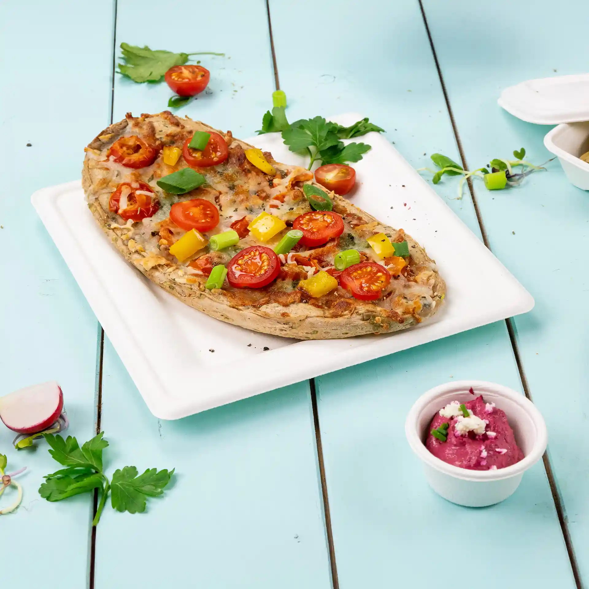 Piatto quadrato bianco in canna da zucchero con una pizza con pomodori, peperoni e cipollotti, accanto a una piccola tazza di salsa.