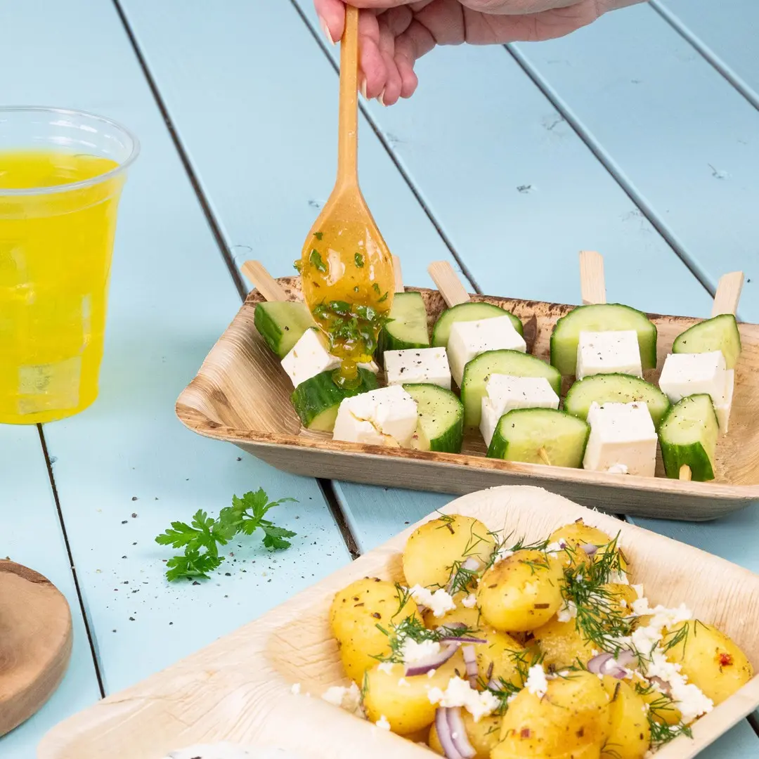 Spiedini di legno con cetriolo e cubetti di formaggio, serviti con patate speziate e una bevanda.