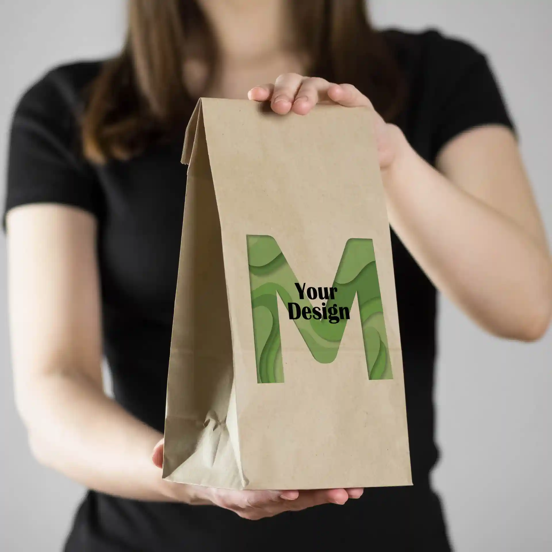 Busta di carta marrone con design verde "M", tenuta da una persona in una maglietta nera.