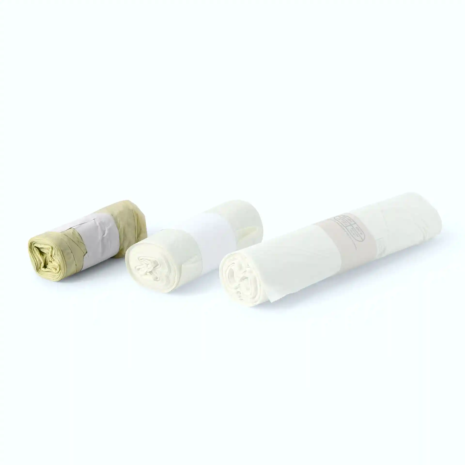 Tre rotoli di sacchetti bio trasparenti in PLA, ciascuno arrotolato e fissato con elastici.