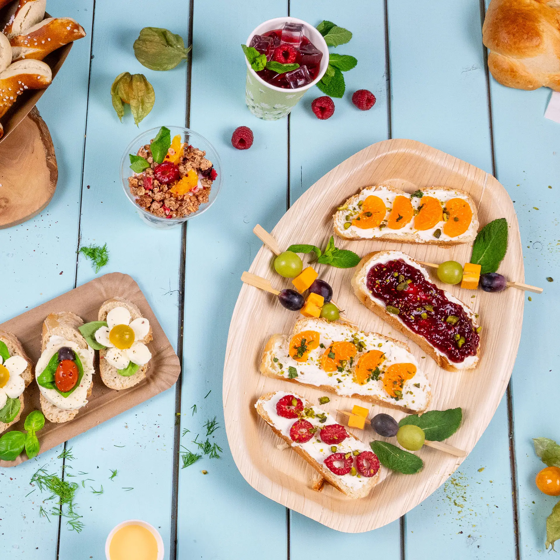 Un vassoio in foglia di palma con vari stuzzichini, inclusi formaggio cremoso guarnito con frutta, disposti elegantemente; frutta e bevande nei paraggi.