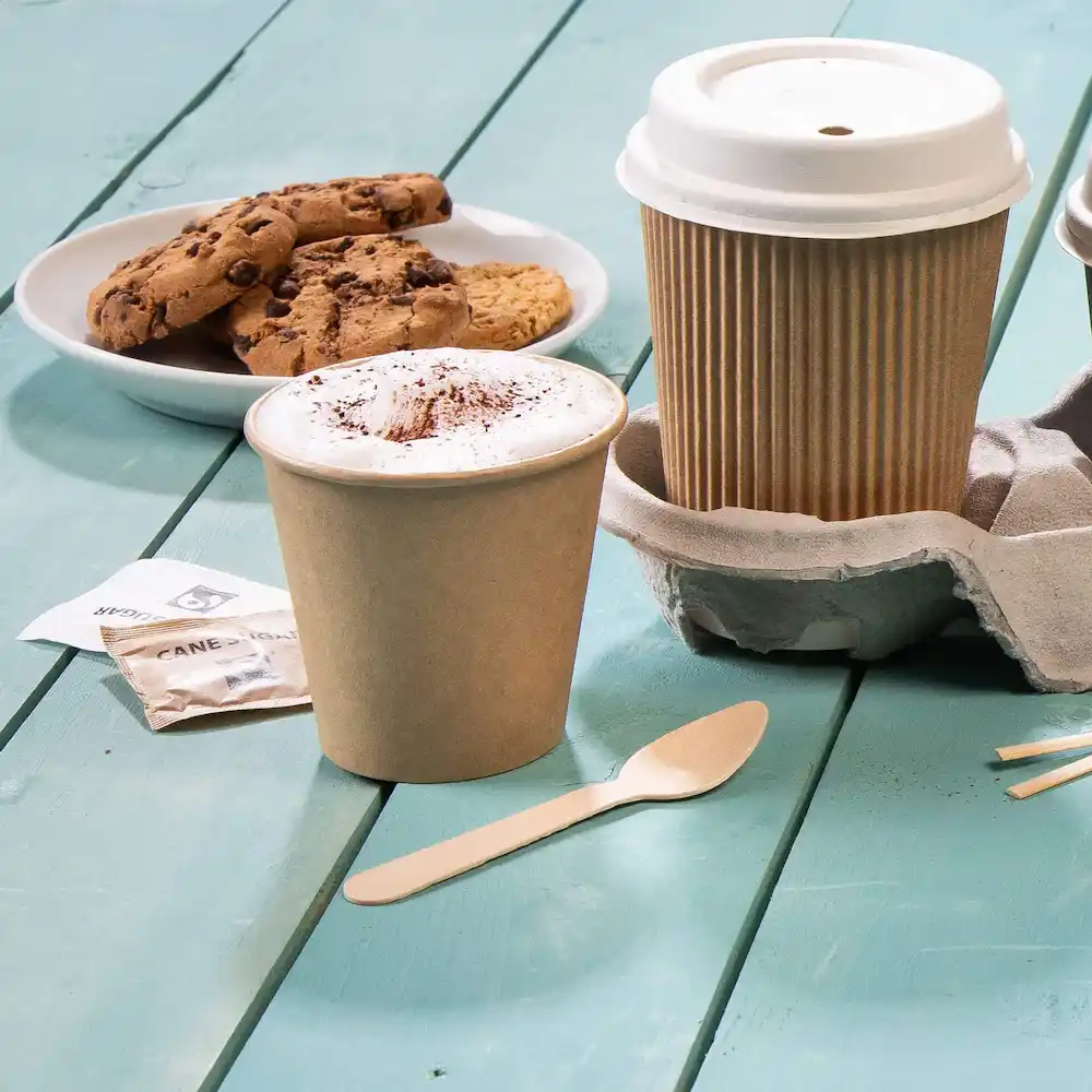 Tazza da caffè marrone con schiuma e cacao, piatto di biscotti, cucchiaio di legno e portacup su una superficie in legno blu.