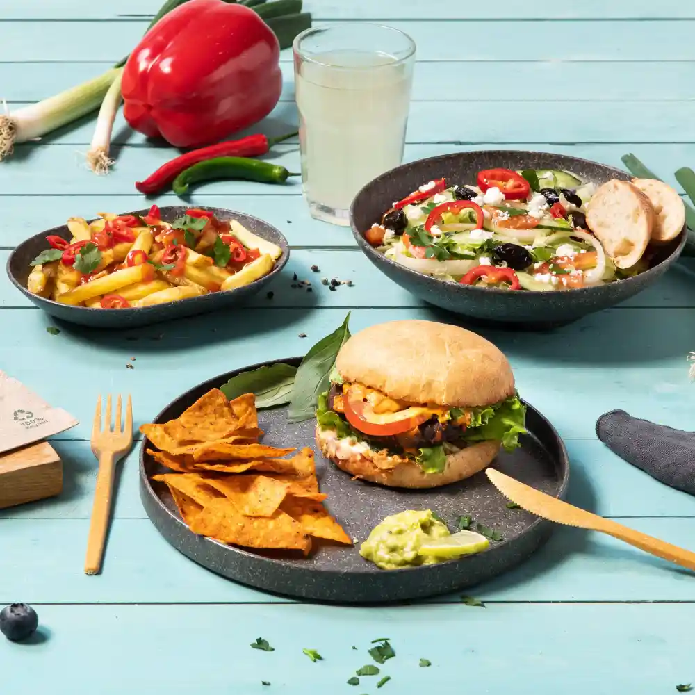 Un burger con lattuga, pomodoro e salsa, servito con tortilla chips e guacamole, insieme a un'insalata e patatine.