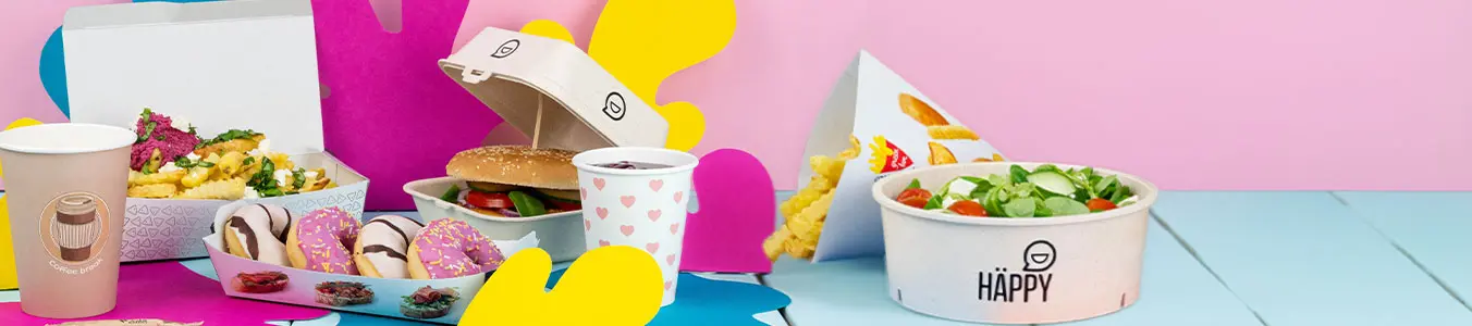 Disponga di fast food da asporto con un hamburger, patatine, ciotola di insalata colorata, salsa e una bevanda su una superficie blu.